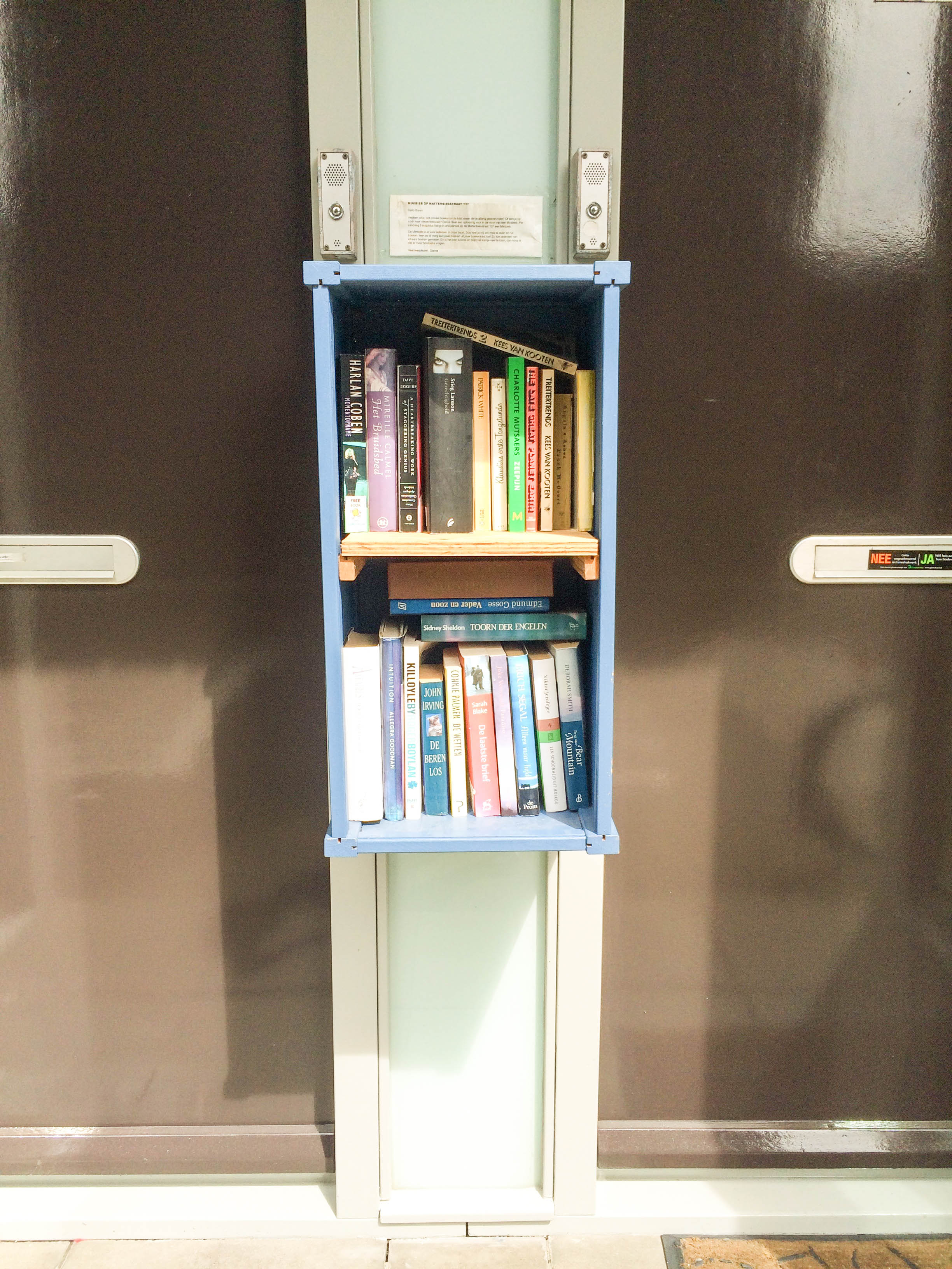 this micro bookshelf between apartment doors in Amsterdam is the definition of a tiny free public library, full of books in English and Dutch