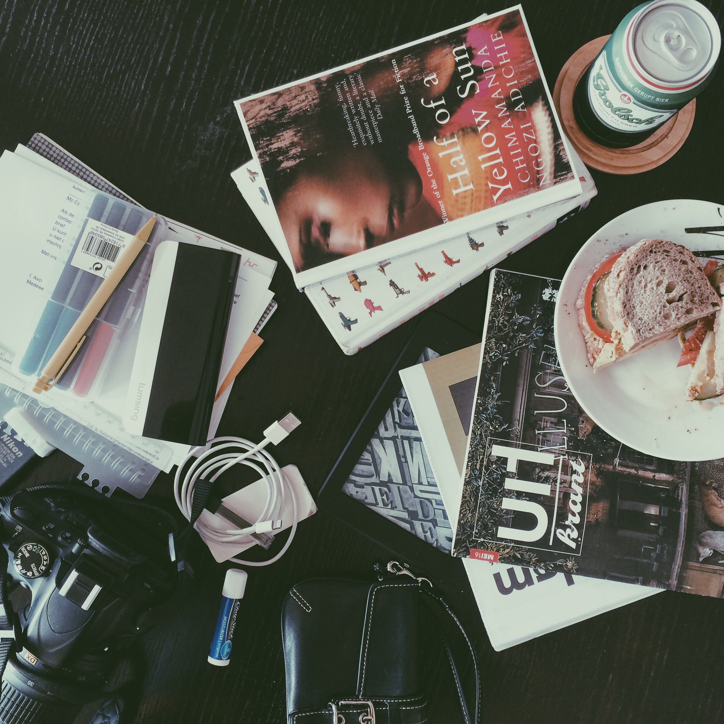 after a trip to the library, I dumped the contents of my bag on to the table. Pictured here: Chimamanda Ngozi Adichie's Half of a Yellow Sun, Charles Yu's How to Live Safely in a Science Fictional Universe, Nikon camera, proofreading pens, Grolsch, sandwich